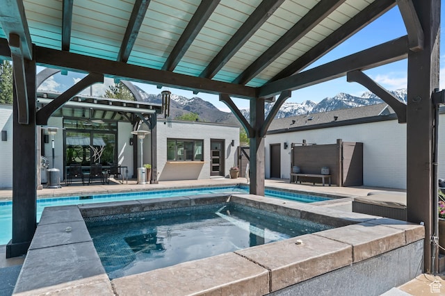 pool featuring a patio, an in ground hot tub, and a mountain view