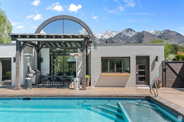 rear view of property with a mountain view, a patio, an outdoor pool, and brick siding
