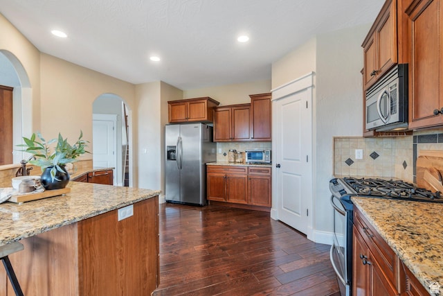 2797 W Fox Hunters Loop, Lehi, UT 84043 - kitchen with appliances with stainless steel finishes, light stone counters, arched walkways, brown cabinetry, and dark wood-style floors
