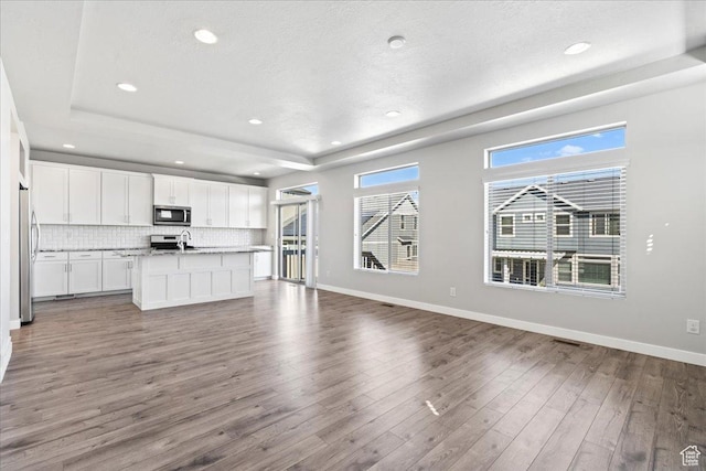 4264 W Abbey Bend Ln, Herriman, UT 84096 - unfurnished living room featuring a tray ceiling, wood finished floors, baseboards, recessed lighting, and a sink