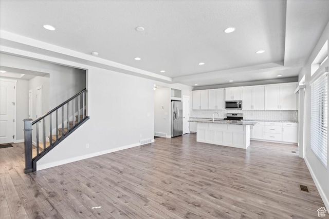 4264 W Abbey Bend Ln, Herriman, UT 84096 - kitchen with appliances with stainless steel finishes, a tray ceiling, white cabinetry, light wood-type flooring, and tasteful backsplash