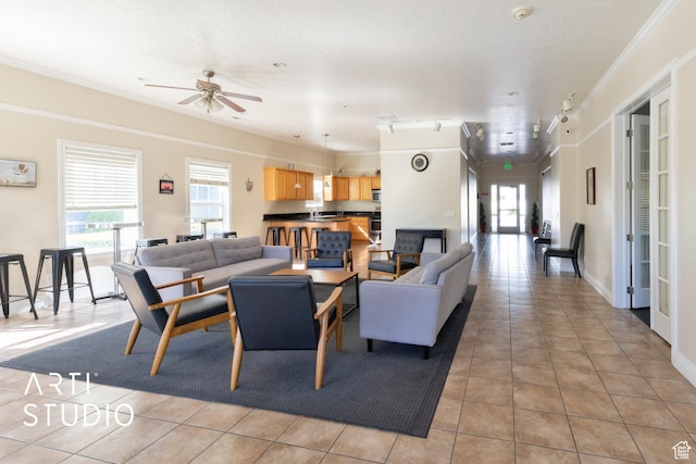 living area with a ceiling fan, baseboards, ornamental molding, and light tile patterned floors