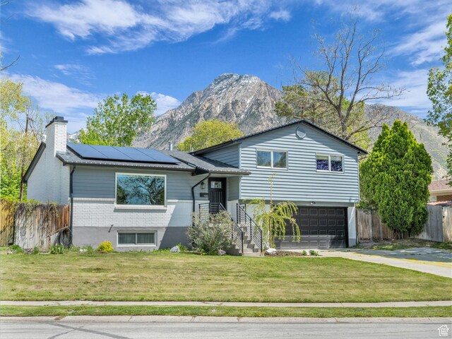 tri-level home with roof mounted solar panels, fence, a mountain view, and a front lawn