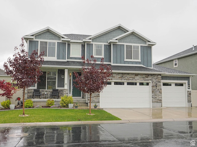 craftsman-style home featuring covered porch, stone siding, a front yard, board and batten siding, and driveway