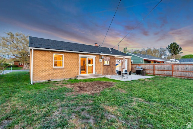 1072 S 1400 W, Salt Lake City, UT 84104 - back of property at dusk featuring fence, brick siding, entry steps, a lawn, and a patio