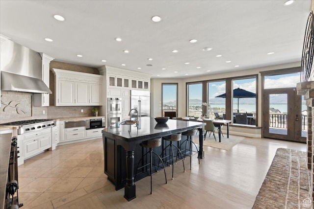 3630 S Panorama Dr W, Saratoga Springs, UT 84045 - kitchen featuring wall chimney range hood, a breakfast bar, a sink, built in appliances, and decorative backsplash