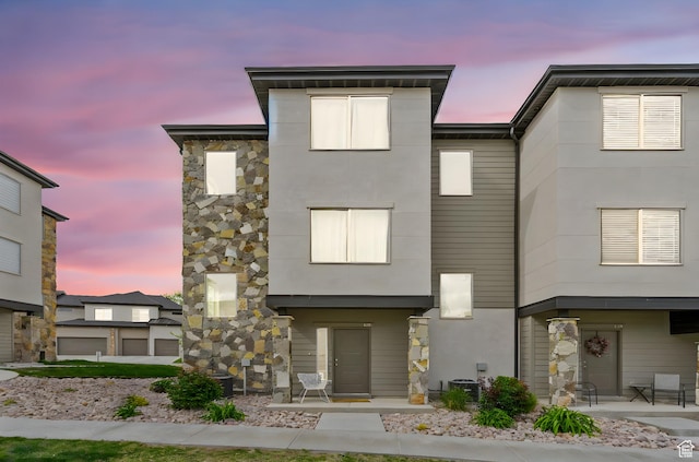 contemporary home with stucco siding, central AC, and stone siding