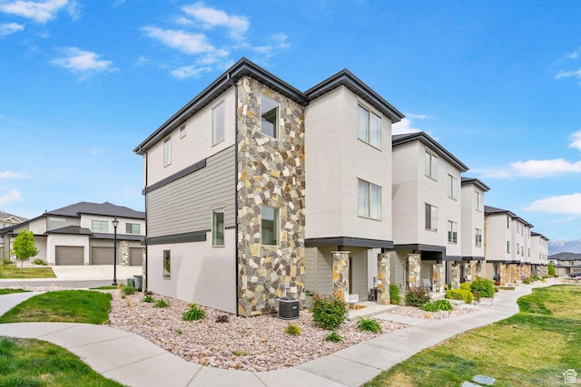 exterior space with central AC unit, a residential view, a front lawn, and stone siding