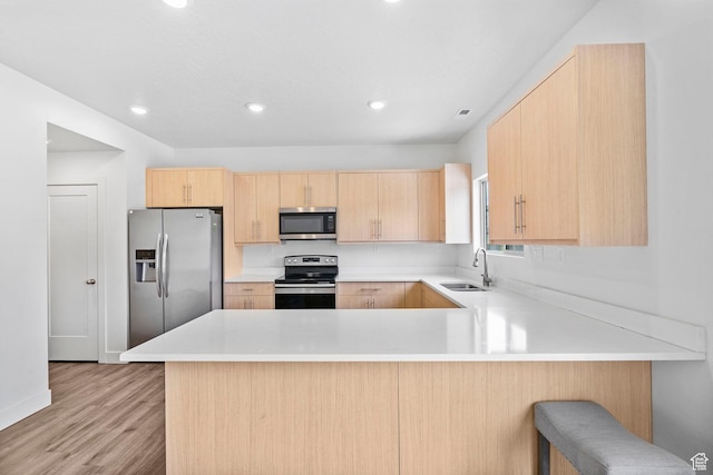 kitchen featuring a peninsula, light brown cabinetry, a sink, light wood finished floors, and stainless steel appliances
