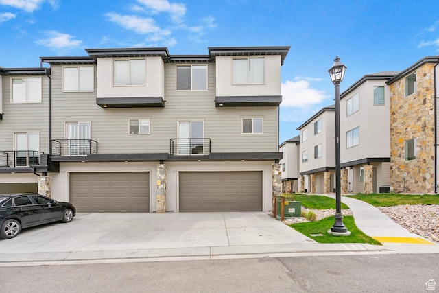multi unit property featuring an attached garage, a balcony, driveway, and cooling unit