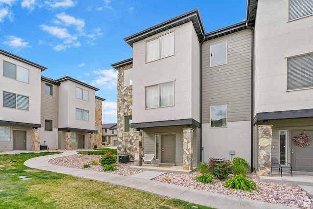 exterior space featuring central AC unit, a residential view, stucco siding, and stone siding