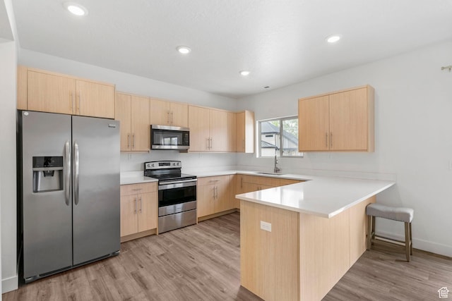 kitchen with light brown cabinetry, a sink, light wood finished floors, stainless steel appliances, and a peninsula