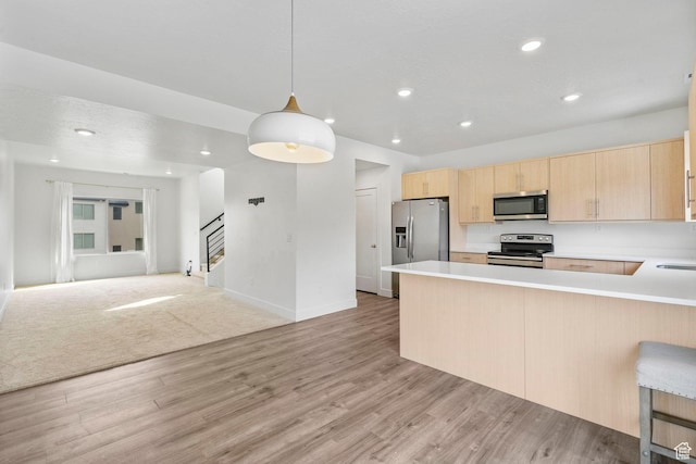 kitchen featuring light countertops, a peninsula, open floor plan, light brown cabinets, and stainless steel appliances