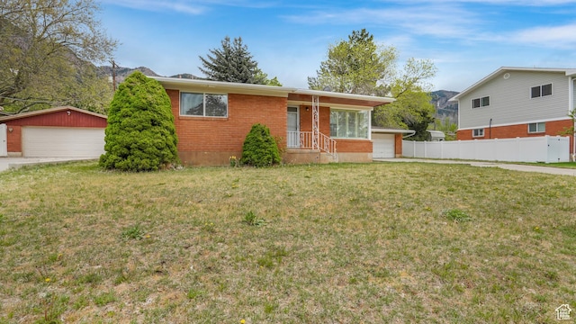 view of front facade featuring fence, a detached garage, brick siding, and a front yard