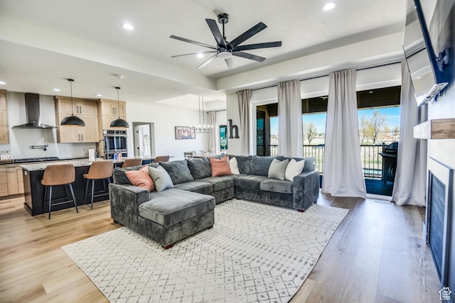 living room featuring recessed lighting, light wood-style flooring, ceiling fan with notable chandelier, and a fireplace