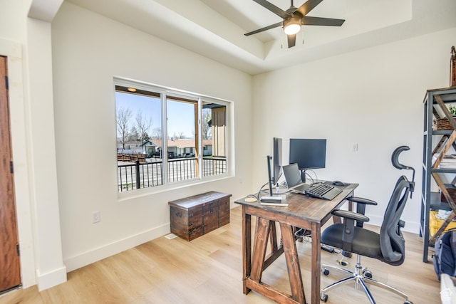 home office with light wood-type flooring, baseboards, ceiling fan, and a tray ceiling
