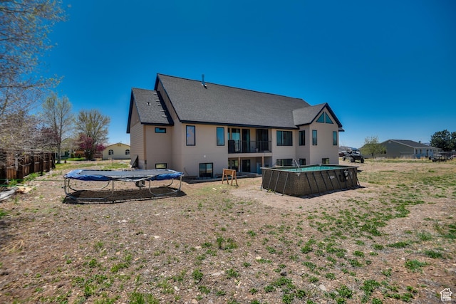 back of house with fence, a fenced in pool, a balcony, and roof with shingles