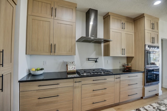 kitchen featuring wall chimney range hood, stainless steel appliances, dark countertops, and light brown cabinets