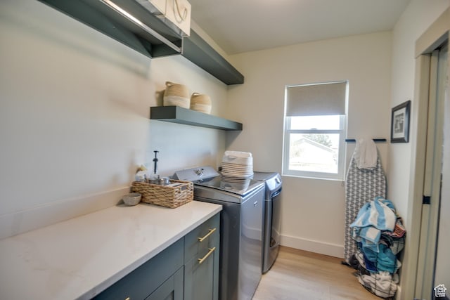 clothes washing area with baseboards, light wood-type flooring, cabinet space, and washing machine and clothes dryer