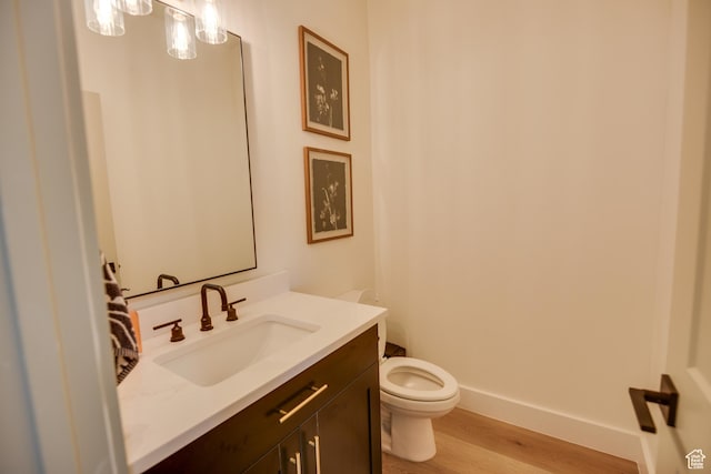 half bathroom featuring vanity, baseboards, toilet, and wood finished floors