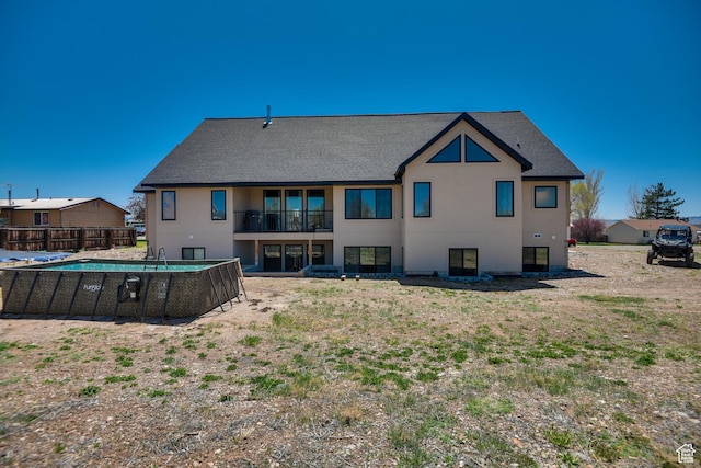 rear view of property featuring a fenced in pool, a shingled roof, stucco siding, and a balcony