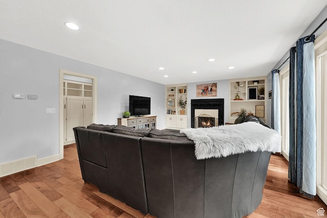 5078 S Iroquois Way E, Ogden, UT 84403 - living area with built in features, a warm lit fireplace, light wood-style flooring, and visible vents