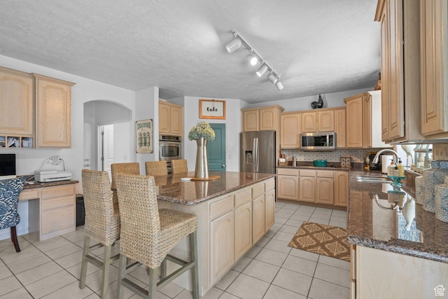 6272 S Lake Fork Cir, Taylorsville, UT 84129 - kitchen featuring a kitchen island, arched walkways, a sink, light tile patterned floors, and stainless steel appliances
