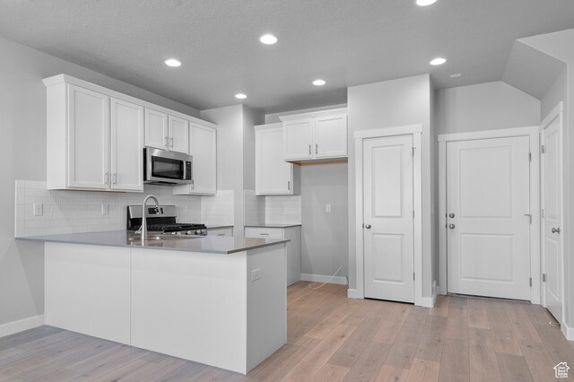 6589 W Bannon St, West Jordan, UT 84081 - kitchen featuring a peninsula, light wood-type flooring, white cabinetry, tasteful backsplash, and appliances with stainless steel finishes