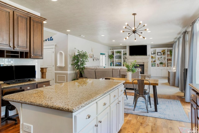 11282 S Alpine Creek Way S, Jordan, UT 84095 - kitchen with a glass covered fireplace, open floor plan, light wood-type flooring, a chandelier, and light stone counters
