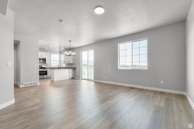 6628 W Spring Snow Ln, Herriman, UT 84096 - unfurnished living room with a chandelier, a sink, baseboards, light wood finished floors, and a textured ceiling