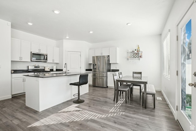 kitchen with appliances with stainless steel finishes, wood finished floors, a wealth of natural light, and dark countertops