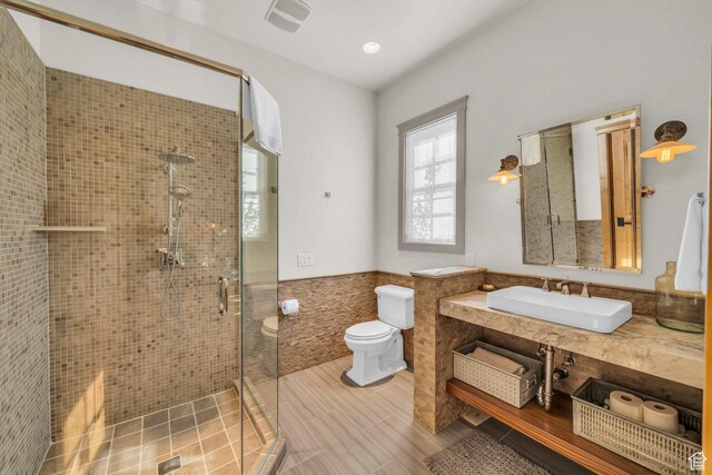 bathroom featuring visible vents, tile walls, a shower stall, a wainscoted wall, and toilet