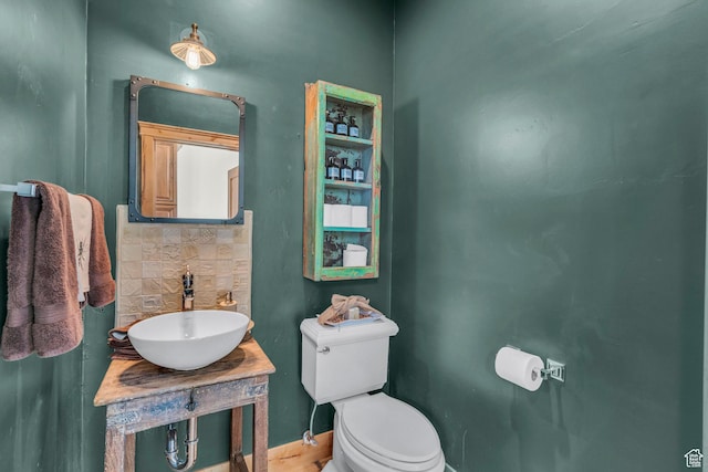 bathroom with wood finished floors, toilet, baseboards, tasteful backsplash, and a sink