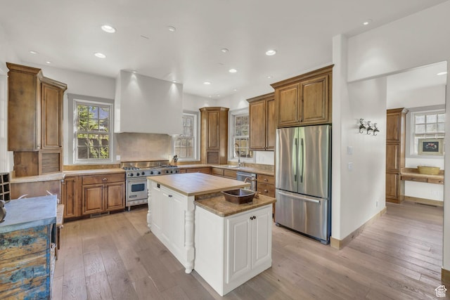 kitchen featuring brown cabinetry, light wood-style flooring, appliances with stainless steel finishes, and range hood