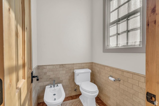 bathroom featuring a bidet, tile walls, tile patterned flooring, wainscoting, and toilet