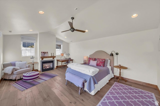 bedroom featuring a glass covered fireplace, a ceiling fan, baseboards, wood finished floors, and lofted ceiling