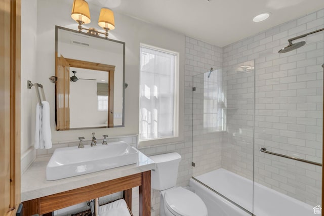 bathroom featuring visible vents, vanity, toilet, tile walls, and bath / shower combo with glass door