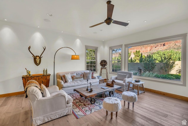 living room featuring baseboards, a ceiling fan, and light wood finished floors