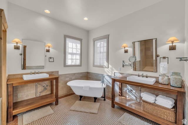 full bath featuring a sink, a freestanding tub, a wainscoted wall, and tile walls
