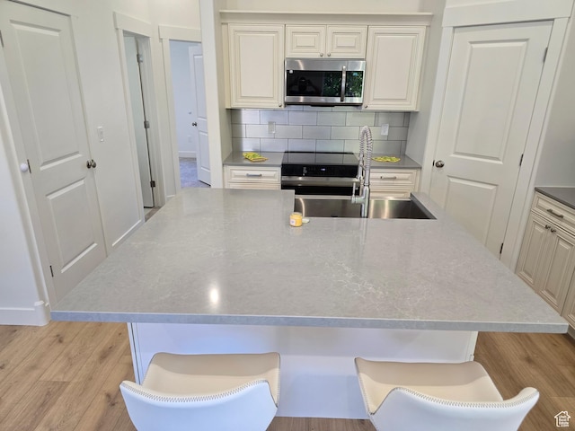 92 N 300 W, American Fork, UT 84003 - kitchen featuring stainless steel microwave, a sink, light wood finished floors, tasteful backsplash, and a kitchen island with sink