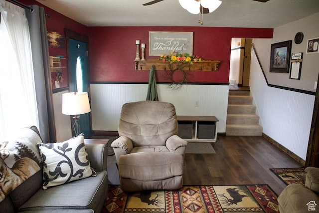 living area with stairs, wood finished floors, baseboards, a wainscoted wall, and a ceiling fan