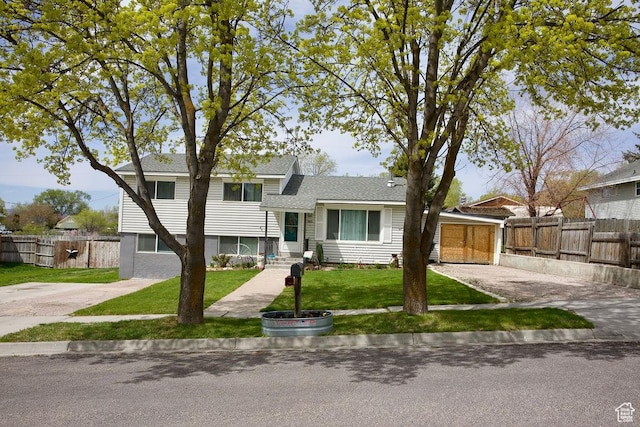 split level home with fence, roof with shingles, and a front yard