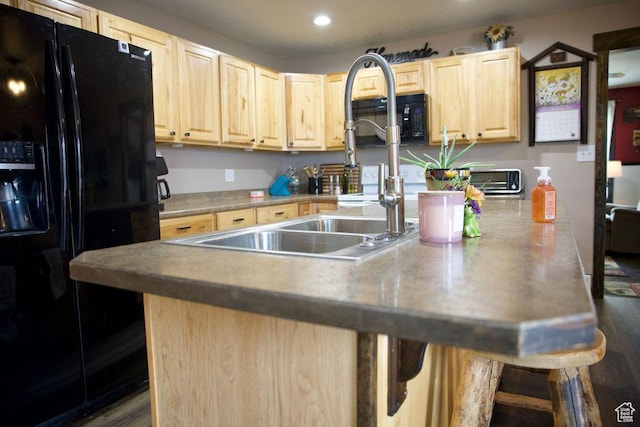 kitchen with a breakfast bar area, a sink, black appliances, light brown cabinets, and recessed lighting
