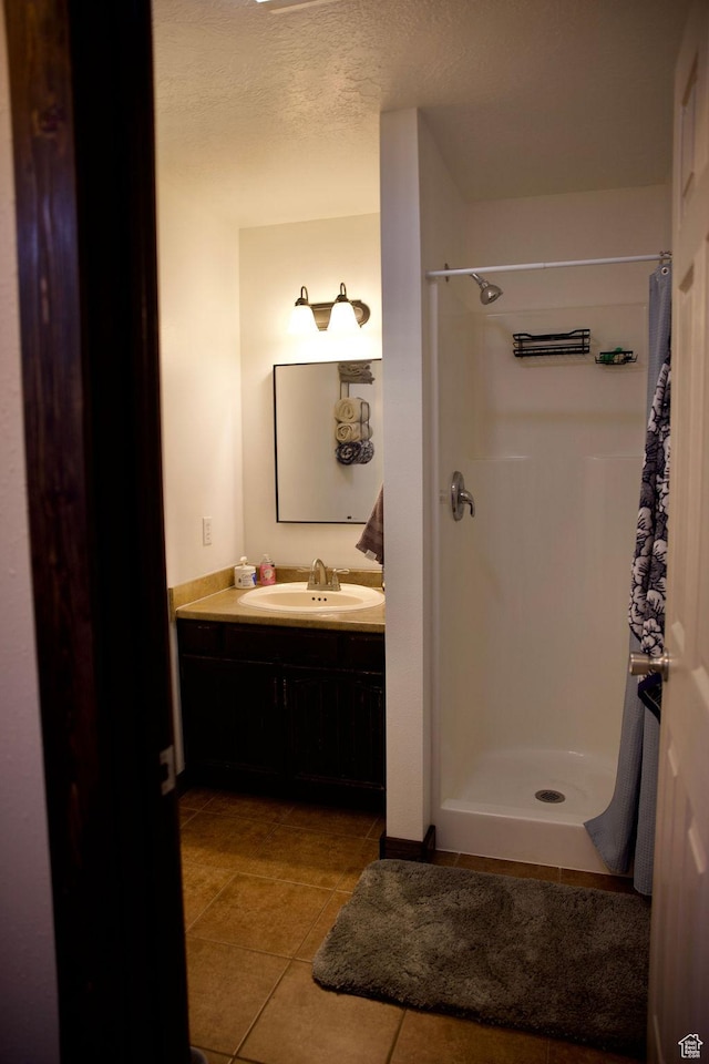 full bath with tile patterned flooring, a textured ceiling, vanity, and a shower stall