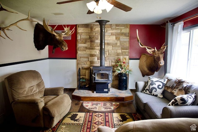 living room with wainscoting, a ceiling fan, a wood stove, and wood finished floors
