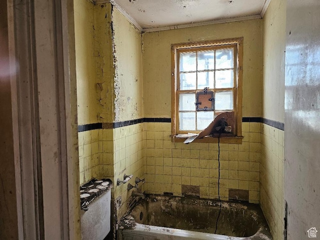 bathroom with a bathing tub, crown molding, tile walls, and a wainscoted wall