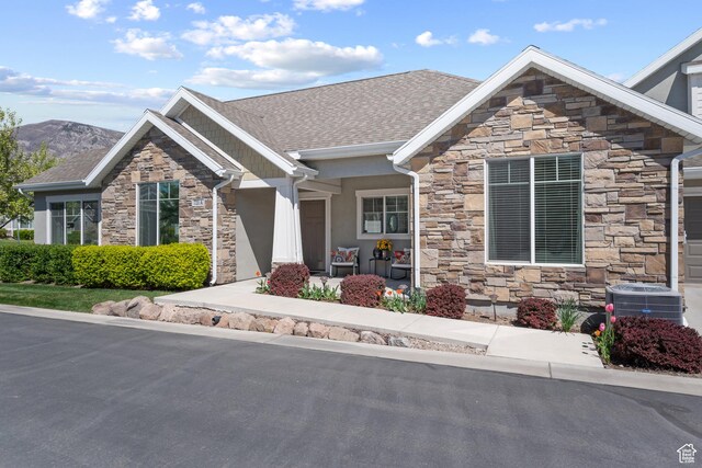 view of front of property with a porch, central AC, stone siding, and stucco siding