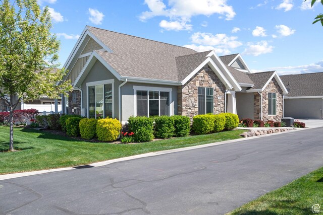 view of front of property featuring roof with shingles, a front lawn, stone siding, and stucco siding