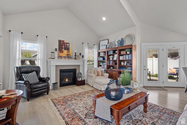 living room with a glass covered fireplace, high vaulted ceiling, and light wood finished floors