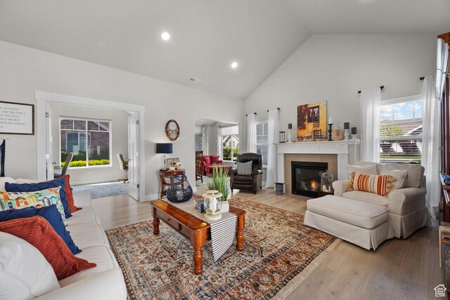 living room featuring visible vents, high vaulted ceiling, light wood-type flooring, recessed lighting, and a fireplace with flush hearth